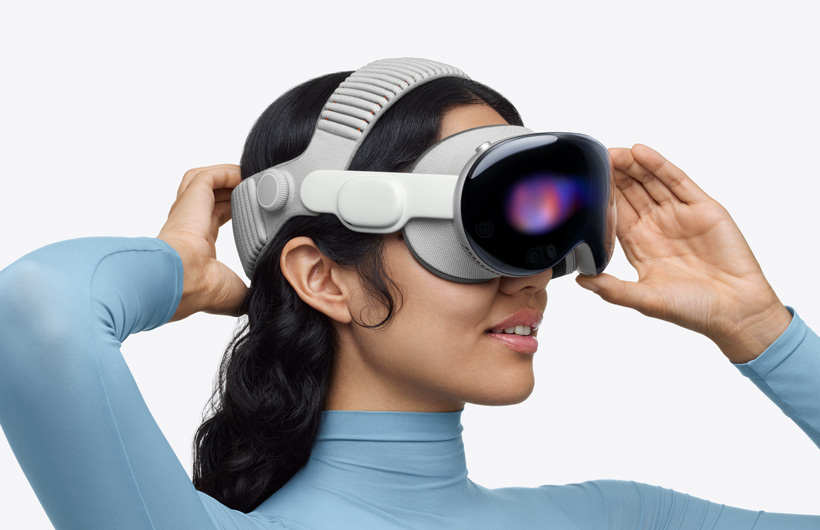 デュアルニットバンドを取りつけたApple Vision Proを装着した人物。上部のバンドが頭の上に装着されている。片方の手が頭の後ろにある下部のバンド上に置かれ、もう片方の手はアルミニウムアロイのフレーム上に置かれている