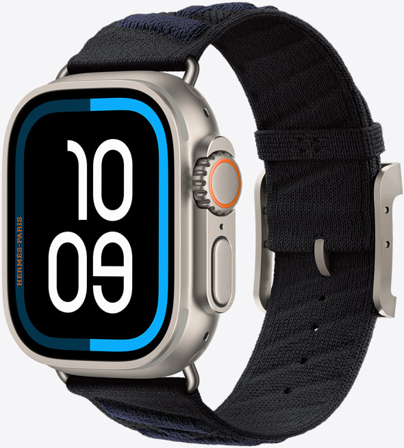ナチュラルチタニウムケースのApple Watch Hermès Ultra 3。エッジからエッジまで広がるディスプレイ、丸みを帯びた四隅。右側面の外観に、Digital Crown、マイク、少し突き出たサイドボタンが見えている。Maritimeのデジタル文字盤（時刻の数字は10 09）。アンメールストラップとの組み合わせ、カラーは黒/ブルー・ニュイ、黒地に、ダークブルーの立体的なストライプが斜めに入っている。ポリアミドのニット素材、中央に調節用の穴があり、ナチュラルカラーのチタニウム製バックルと金具が付いている