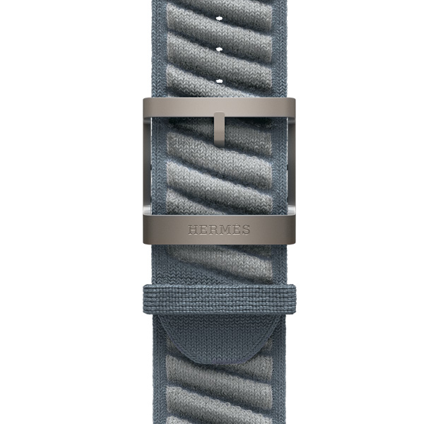 Apple Watch Hermès Ultra 3アンメールストラップ。カラーはブルー・グリ/ブルー・グラシエ、ブルーグレイのベースカラーにライトグレイの立体的なストライプが斜めに入っている。ポリアミドのニット素材、中央に調節用の穴があり、Hermèsの刻印が入ったナチュラルカラーのチタニウム製バックルが付いている