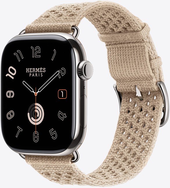 シルバーチタニウムケースのApple Watch Hermès Series 11。鏡面仕上げ、エッジからエッジまで広がるディスプレイ、丸みを帯びた四隅。右側面の外観に、Digital Crown、マイク、サイドボタンが見えている。アナログデザインの文字盤に時針、分針、秒針が表示されている。アルジル（ベージュ）のネオ・トリコストラップとの組み合わせ。ポリアミドのニット素材で、中央に調節用の穴があり、シルバーカラーのバックルと金具が付いている