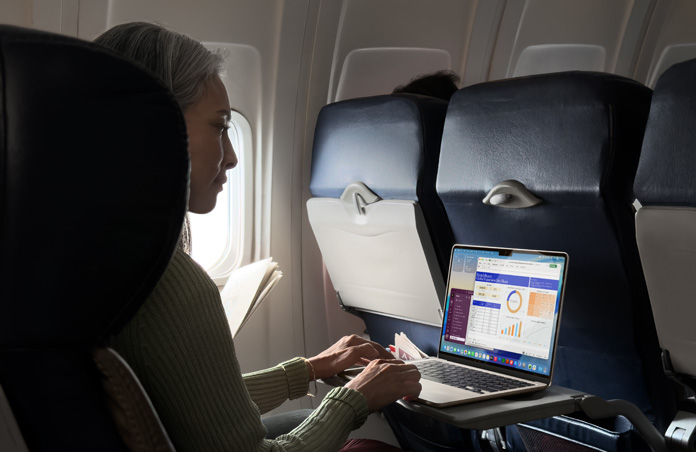 一個人坐在飛機上，使用 MacBook Air 工作